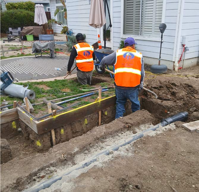 DFM Concrete Construction crew members in safety vests performing excavation and trenching work for a residential backyard project, ensuring precise ground preparation for general contractors
