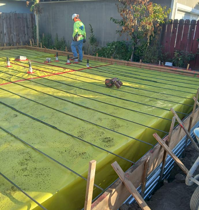 New residential concrete foundation prep featuring a moisture vapor barrier and steel rebar reinforcement grid, with a worker inspecting the structural layout for a durable slab-on-grade build