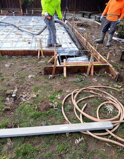 Construction crew member using a hose to pour fresh concrete into the rebar-reinforced formwork for a new foundation slab.