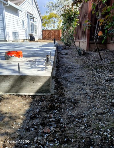 Completed concrete stem wall foundation and slab with anchor bolts and piping penetrations in a residential backyard.