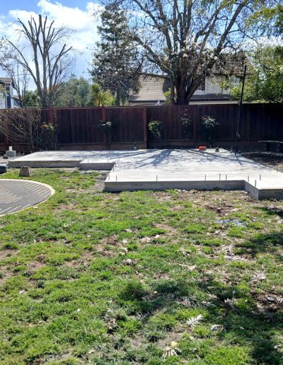 Wide view of a finished, cured concrete slab and foundation pads placed in a residential backyard for a new structure.