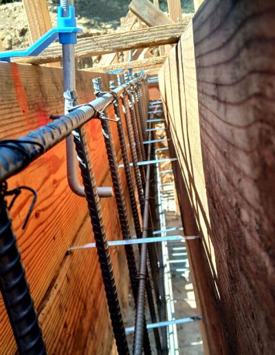 Extremely close-up view of vertical steel rebar reinforcement inside the wooden formwork for a concrete foundation wall.