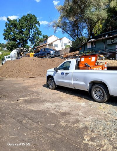 Construction site staging area with a large pile of excavated dirt, a cement mixer, and DFM Concrete's white pickup truck.