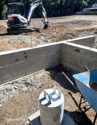 Wide, sunny view of a residential backyard showing a completed, flat concrete slab foundation ready for vertical construction.