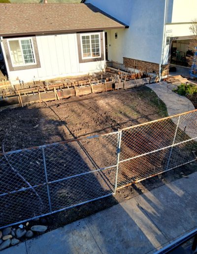 Exterior view of a house showing the fenced off area prepared for a new concrete foundation or room addition project.