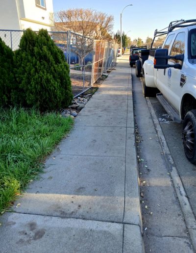 Street-level view of a sidewalk and curb near the work site, showing site fencing and a parked work truck.