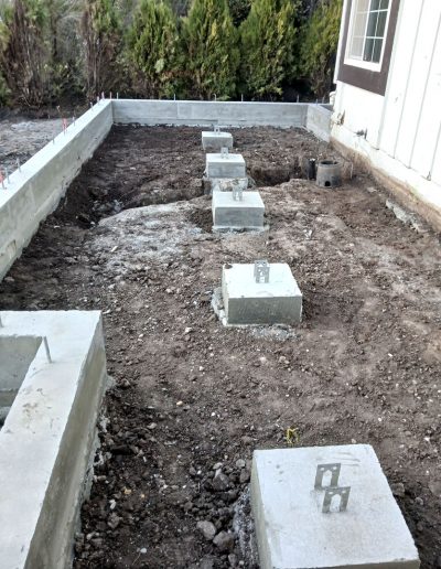 Completed concrete footings and vertical piers for a new building addition foundation on a residential property.