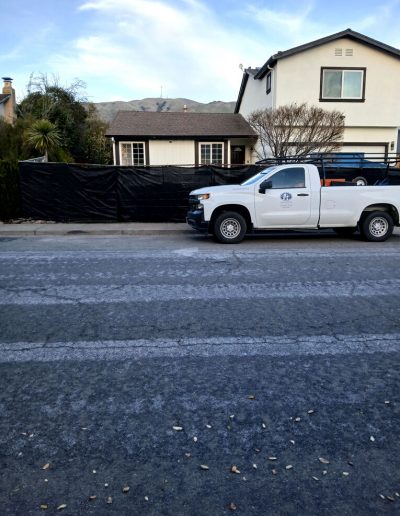 Wide street view of a residential house with a white pickup truck parked outside, showing the construction area obscured by black screening.