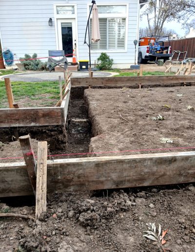 Close-up of deep trenching and wooden formwork being set up for a concrete foundation footing next to a residential home.
