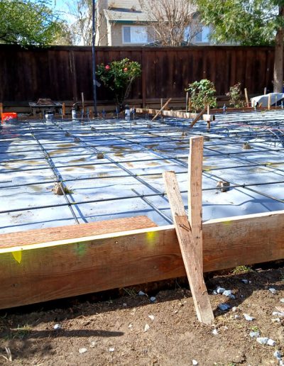 Plastic sheeting (vapor barrier) laid over the prepared ground, with a grid of steel rebar mesh secured on blocks for a concrete slab foundation.
