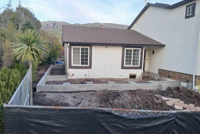 How Much Does a Concrete Driveway Cost: Concrete slab-on-grade foundation preparation featuring a yellow moisture vapor barrier and a steel rebar reinforcement grid, with a worker inspecting the structural layout before pouring