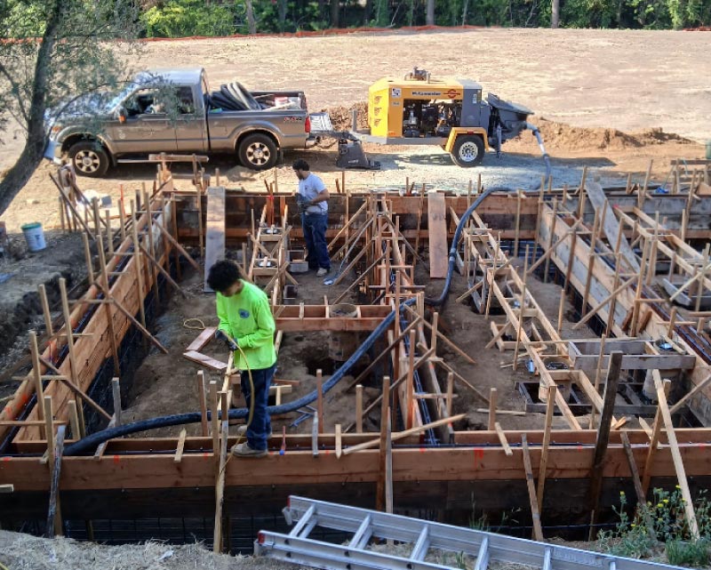 DFM Concrete crew members meticulously preparing a complex wooden formwork for a crawl space foundation on a residential job site for a new ADU construction, featuring a professional concrete pump and service truck in the background.